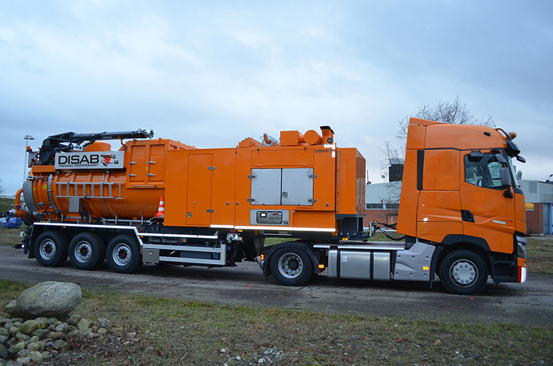 Orange DISAB Centurion™ LN20 industrial vacuum unit mounted on a four-axle truck chassis, parked on a grassy area, designed for high-performance suction and safe transport of wet and dry materials.