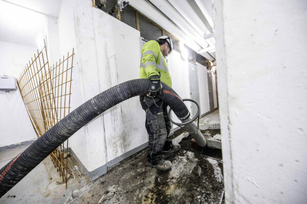 Operator in safety gear using a curved industrial vacuum hose inside a building, connected to a DISAB Centurion™ LN30 unit, demonstrating precision cleaning of hazardous or fine materials in tight indoor spaces.